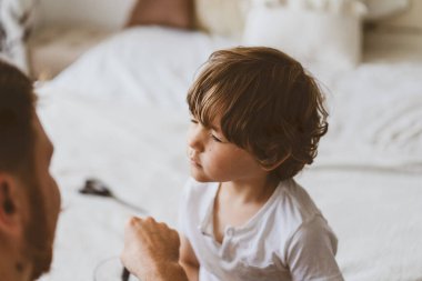 Baba odada oğlunun saçını kesiyor. Karantina sırasındaki aile, makas ve erkek ellerinde tarak.