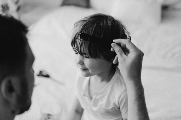 Black and white photo. Father cuts her son hair in the room. Family during quarantine, Scissors and a comb in male hands — Stock Photo, Image