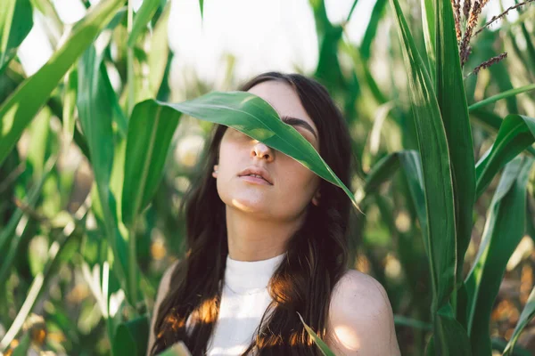 Ein junges Mädchen in einem Maisfeld. Trend - geschlossenes Mädchengesicht mit Maisblättern. Einheit mit der Natur. — Stockfoto