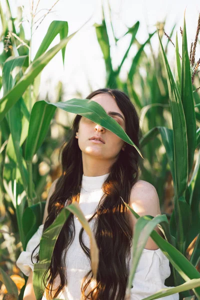 A young girl in a cornfield. Trend - closed girl face with corn leaves.  Unity with nature. — Stock Photo, Image