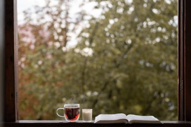 Bir fincan sıcak çay ve eski bir pencere eşiğinde açık bir kitap.