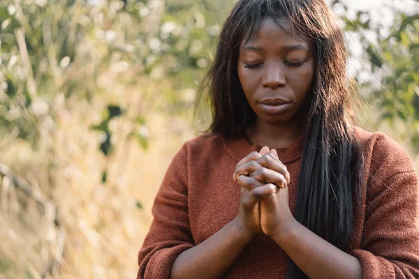Afro Girl chiuse gli occhi, pregando. Mani giunte nel concetto di preghiera per la fede, la spiritualità e la religione Foto Stock Royalty Free
