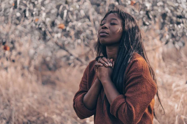 A Afro Girl fechou os olhos, rezando. Mãos dobradas no conceito de oração pela fé, espiritualidade e religião Imagens De Bancos De Imagens
