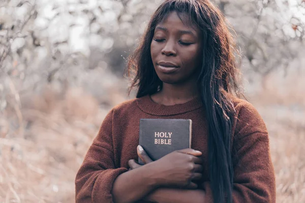 Christian afro ragazza tiene la Bibbia nelle sue mani. Leggere la Sacra Bibbia. Concetto di fede. Fotografia Stock