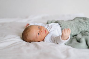 Yeni doğmuş bebek yumuşak bir battaniyenin altında uzanıyor, sakin bir sabah boyunca masumiyet ve merak dolu bir anı yakalıyor.
