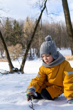 Child having fun in the snow, wearing winter clothing in snowy landscape during daytime. Child with a big smile surrounded by snowy trees and a clear blue sky.
