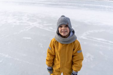 Child having fun in the snow, wearing winter clothing in snowy landscape during daytime. Child with a big smile surrounded by snowy trees and a clear blue sky.