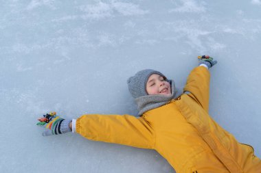 Child having fun in the snow, wearing winter clothing in snowy landscape during daytime. Child with a big smile surrounded by snowy trees and a clear blue sky.