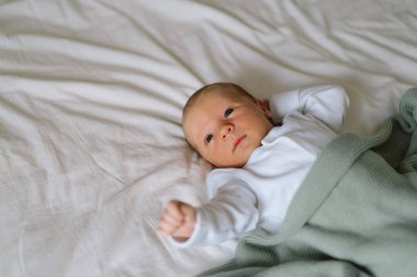 Yeni doğmuş bebek yumuşak bir battaniyenin altında uzanıyor, sakin bir sabah boyunca masumiyet ve merak dolu bir anı yakalıyor.