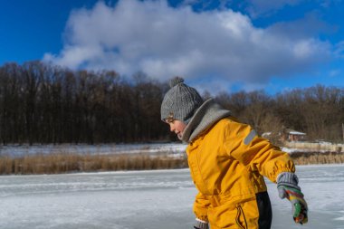 Child having fun in the snow, wearing winter clothing in snowy landscape during daytime. Child with a big smile surrounded by snowy trees and a clear blue sky.