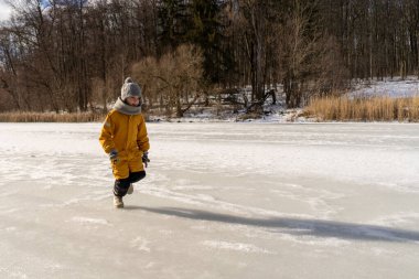 Child having fun in the snow, wearing winter clothing in snowy landscape during daytime. Child with a big smile surrounded by snowy trees and a clear blue sky.