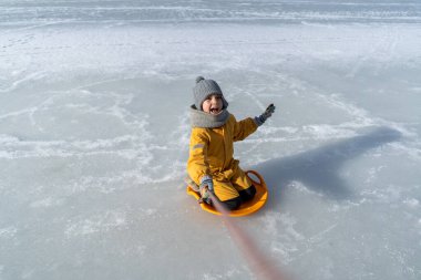 Child having fun in the snow, wearing winter clothing in snowy landscape during daytime. Child with a big smile surrounded by snowy trees and a clear blue sky.