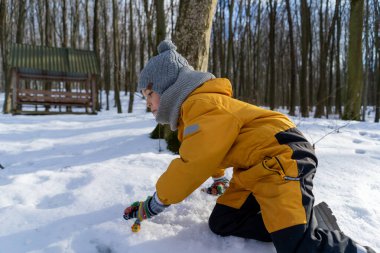 Child having fun in the snow, wearing winter clothing in snowy landscape during daytime. Child with a big smile surrounded by snowy trees and a clear blue sky.