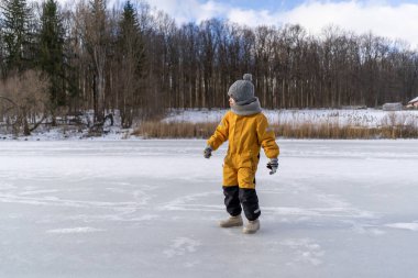 Child having fun in the snow, wearing winter clothing in snowy landscape during daytime. Child with a big smile surrounded by snowy trees and a clear blue sky.