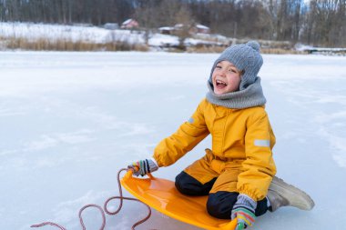 Child having fun in the snow, wearing winter clothing in snowy landscape during daytime. Child with a big smile surrounded by snowy trees and a clear blue sky.