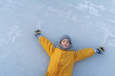 Child having fun in the snow, wearing winter clothing in snowy landscape during daytime. Child with a big smile surrounded by snowy trees and a clear blue sky.