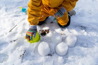 Child having fun in the snow, wearing winter clothing in snowy landscape during daytime. Child with a big smile surrounded by snowy trees and a clear blue sky.