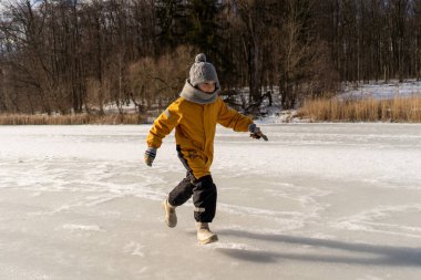 Child having fun in the snow, wearing winter clothing in snowy landscape during daytime. Child with a big smile surrounded by snowy trees and a clear blue sky.