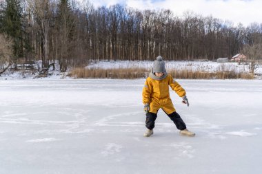 Child having fun in the snow, wearing winter clothing in snowy landscape during daytime. Child with a big smile surrounded by snowy trees and a clear blue sky.