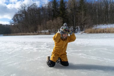 Child having fun in the snow, wearing winter clothing in snowy landscape during daytime. Child with a big smile surrounded by snowy trees and a clear blue sky.