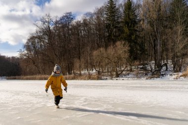 Child having fun in the snow, wearing winter clothing in snowy landscape during daytime. Child with a big smile surrounded by snowy trees and a clear blue sky.