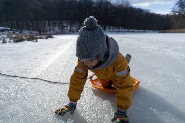 Child having fun in the snow, wearing winter clothing in snowy landscape during daytime. Child with a big smile surrounded by snowy trees and a clear blue sky.