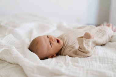 Cute baby lying on a soft white blanket with a calm expression while raising arms. Beautiful portrait of a child. Newborn baby lying on bed