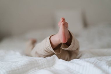 Tiny baby feet peek out from a soft, light-colored blanket on a cozy bed. The peaceful, warm indoor setting creates a serene atmosphere for the sleeping child.