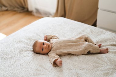 Cute baby lying on a soft white blanket with a calm expression while raising arms. Beautiful portrait of a child. Newborn baby lying on bed