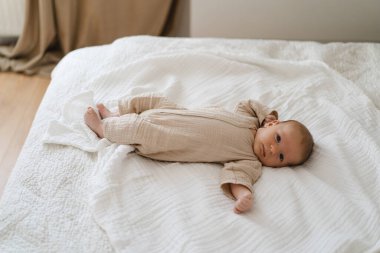 Cute baby lying on a soft white blanket with a calm expression while raising arms. Beautiful portrait of a child. Newborn baby lying on bed