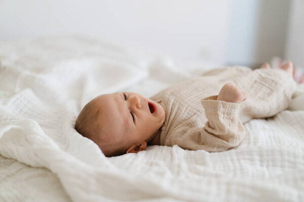 Cute baby lying on a soft white blanket with a calm expression while raising arms. Beautiful portrait of a child. Newborn baby lying on bed