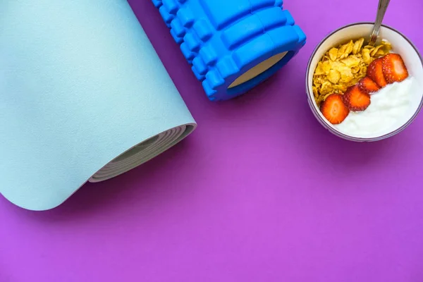 Blue mat for yoga and yoghurt with strawberries and fruits on a purple background