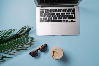 Çalışma alanı: Laptop, palmiye yaprağı, kahve ve çilek mavi bir arka plan üzerinde. Üstten Görünüm, düz yatıyordu, metin için yer