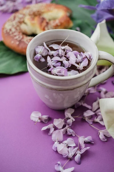 Herbal tea with wisteria, irises, white callas on violet background.