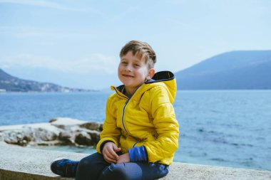 Sevimli gülümseyen çocuk 7 yaşında tek başına denize karşı bir sarı ceketli portresi.