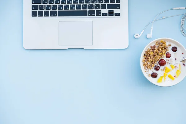 Healthy breakfast before working. Bowl of homemade Granola baked with yogurt aand laptop on blue background