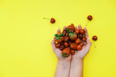 Çilek ve vişne sarı bir arka plan üzerinde eller. Üstten görünüm, düz yatıyordu, kopya alanı