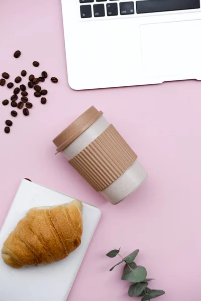 自由职业者家庭办公办公桌与笔记本电脑和毯子工作区 早晨早餐与咖啡和牛角面包在粉红色的背景 顶部看法静物概念 — 图库照片