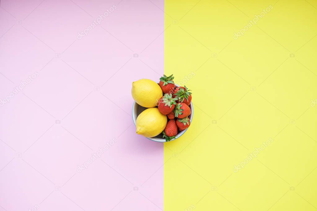 Fresh lemons and strawberries in a bowl on a yellow and pink background. Flat lay, top view