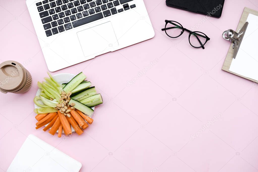 Freelancer home office desk workspace  with laptop and  healthy vegetable snack on pink background. Flat lay, top view still life concept.