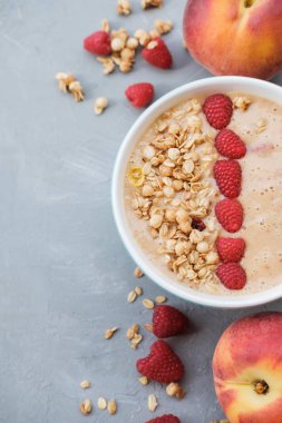 Granola ve gri arka plan üzerinde mavi bir kabın içinde ahududu ile şeftali yüzlü kase. Üstten görünüm. Sağlıklı ve renkli kahvaltı