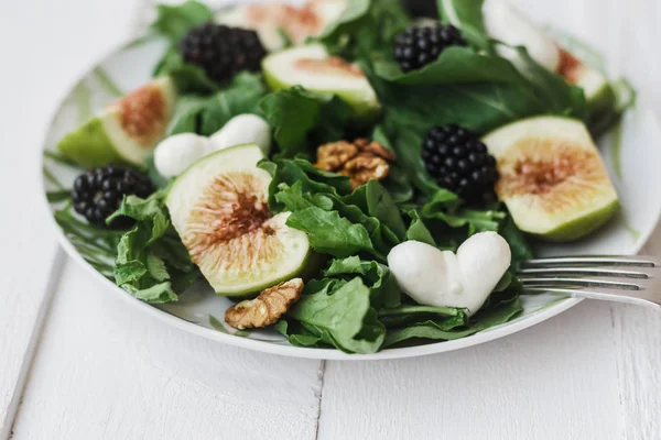 Mozzarella in the shape of heart in Salad with arugula figs blackberry and walnut on white table