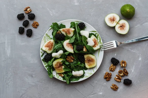 Salad with arugula figs blackberry and walnut on white table. Top view