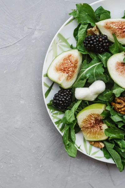 Salad with arugula figs blackberry and walnut on white table. Top view