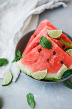 Karpuz dilimleri ve kireç bir plaka üzerinde gri bir arka plan üzerinde