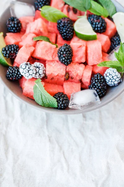Fruit salad from Watermelon slices, frozen blackberry and lime on a plate on white background. Top view, copy space