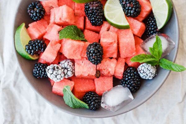 Fruit salad from Watermelon slices, frozen blackberry and lime on a plate on white background. Top view