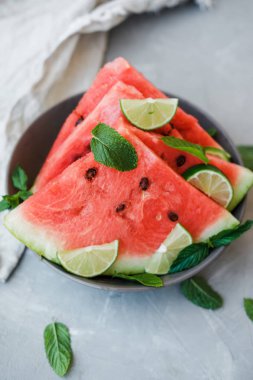 Karpuz dilimleri ve kireç bir plaka üzerinde gri bir arka plan üzerinde