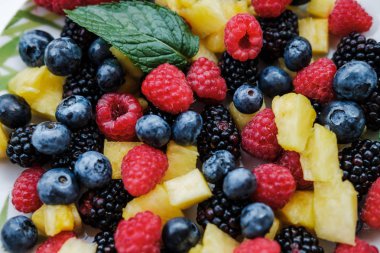 Gökkuşağı renkleri, ananas, böğürtlen, yaban mersini ve ahududu nane ile sağlıklı meyveleri bakış beyaz masa üzerinde plaka üzerinde kapatın
