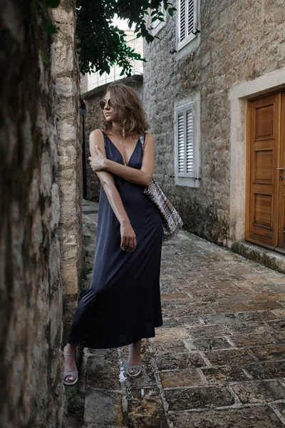 Kıvırcık sarışın genç kadın uzun elbise ve güneş gözlüğü portresi Budva, Karadağ'ın eski şehir etrafında yürür. Yavaş motio